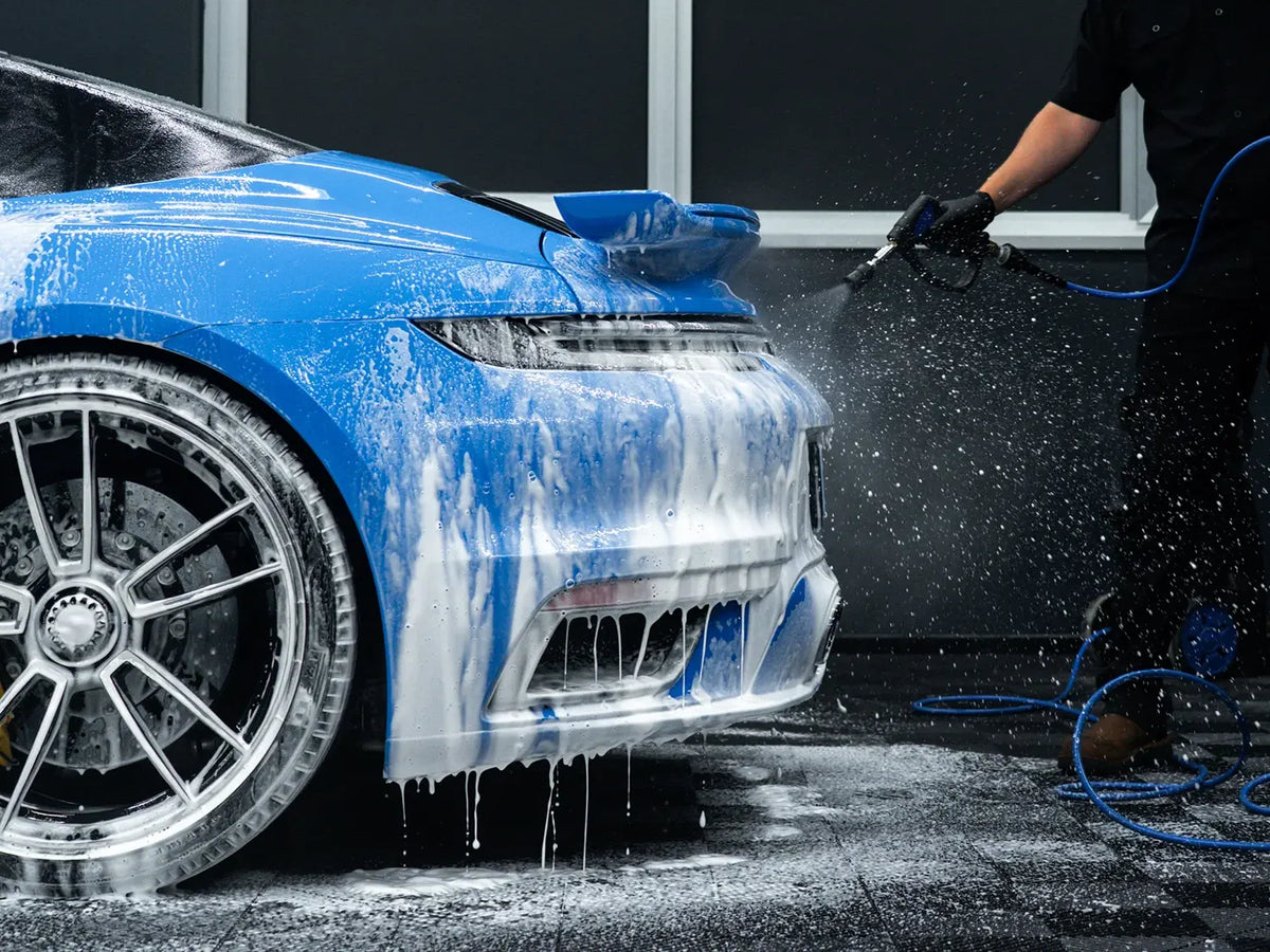 Niebieskie Porsche pokryte pianą podczas mycia wstępnego, detailer spłukuje auto myjką ciśnieniową